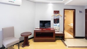 A hotel room with a flat-screen TV, a wooden entertainment unit, a small round table, a beige chair, and a mirror with a bed reflection. - GreenTree Inn Tianjin Hebei District Beining Park Hotel (Tianjin)