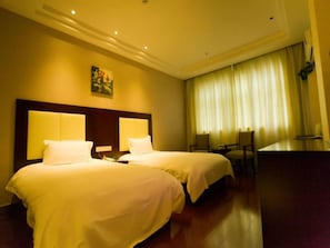 Ein Hotelzimmer mit zwei Betten, einem Schreibtisch und einem großen Fenster mit Vorhängen.