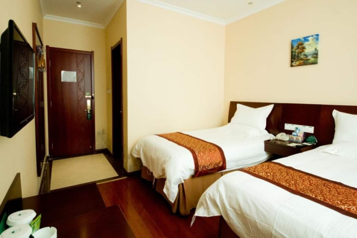 A hotel room with two beds, wooden flooring, a flat-screen TV, and a painting on the wall.