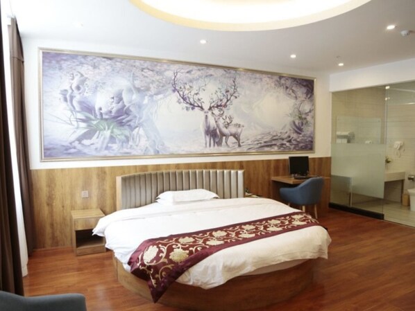 A modern hotel room with a large bed, a desk, and a bathroom visible through a glass partition.