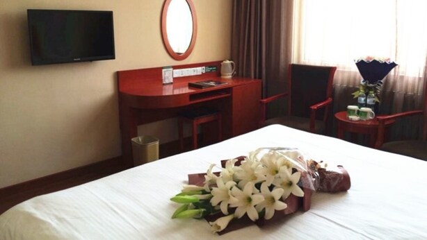 A hotel room with a bed, a desk, a chair, a television, and a window with curtains.