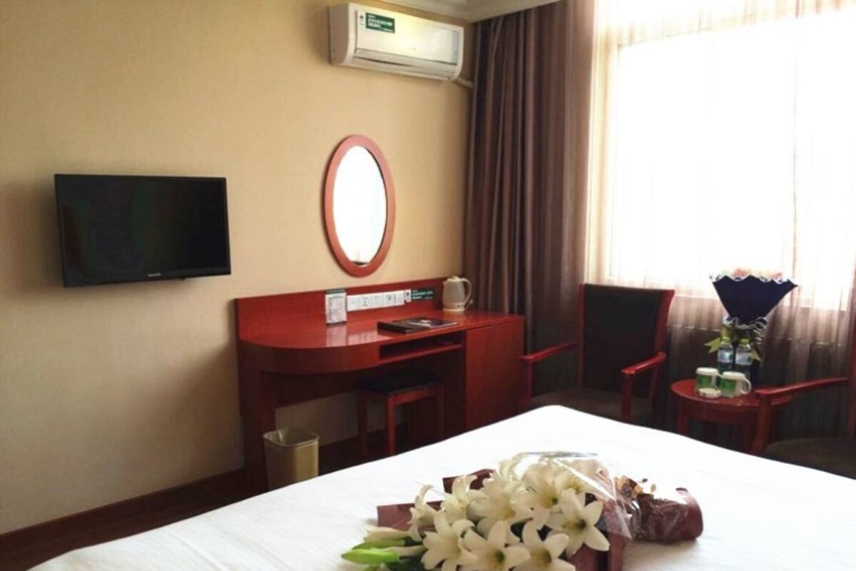 Ein Hotelzimmer mit Bett, Schreibtisch, Stuhl, Fernseher und einem Fenster mit Vorhängen.