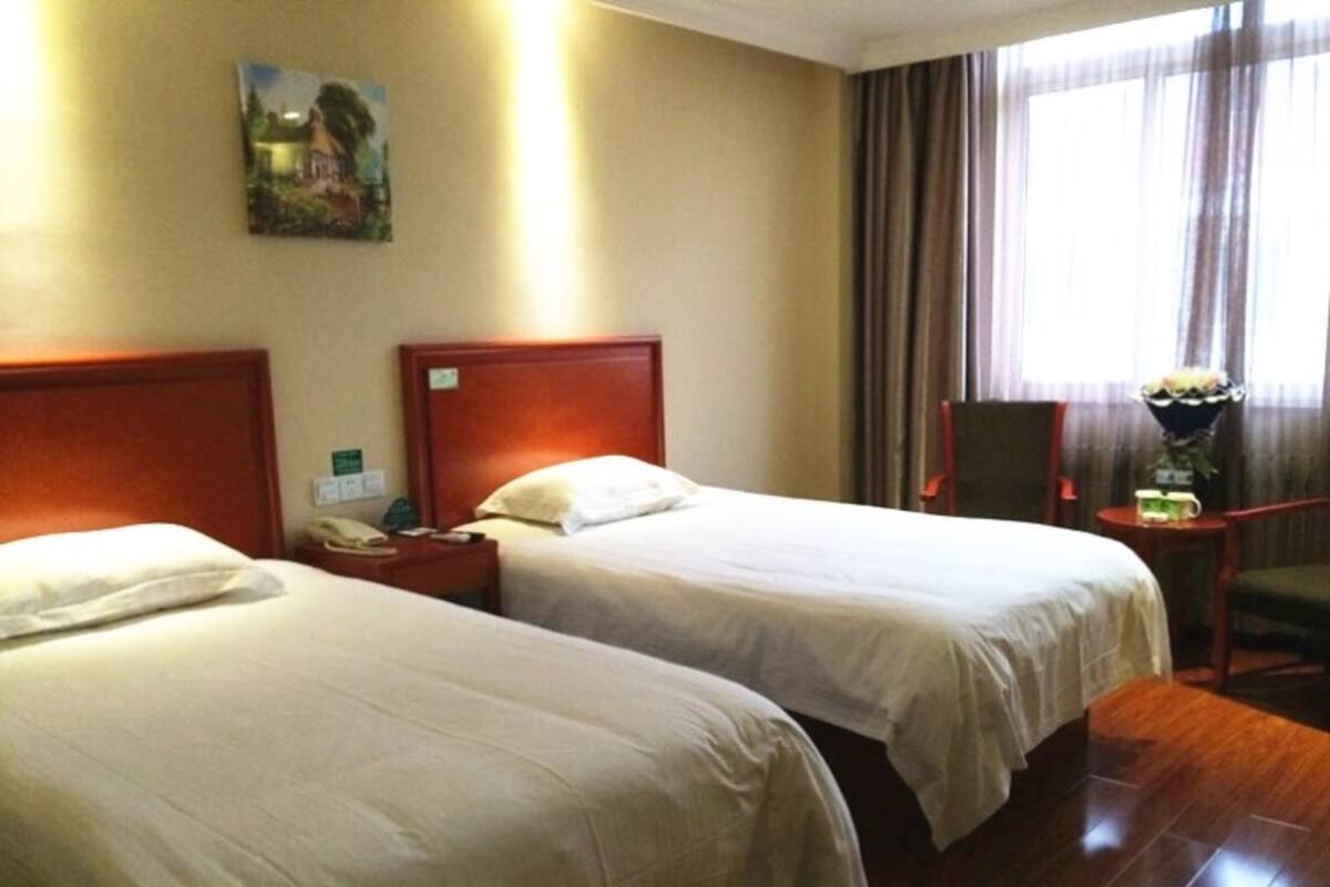 Ein Hotelzimmer mit zwei Betten, einem Nachttisch mit Telefon, einem Sessel und einem Fenster mit Vorhängen.