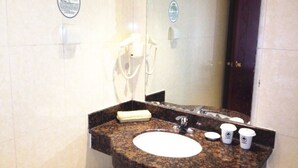 A bathroom with a granite countertop sink, a handheld showerhead, a towel, and a mirror.