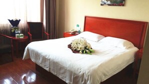 A hotel room with a large bed, a nightstand, a chair, a small table with a vase of flowers, and a painting on the wall.
