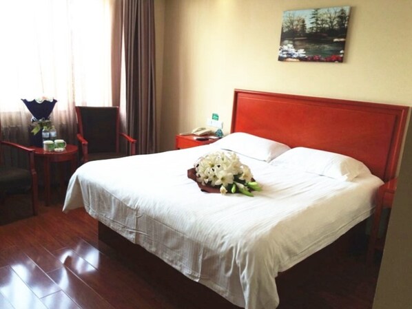 A hotel room with a large bed, a nightstand, a chair, a small table with a vase of flowers, and a painting on the wall.