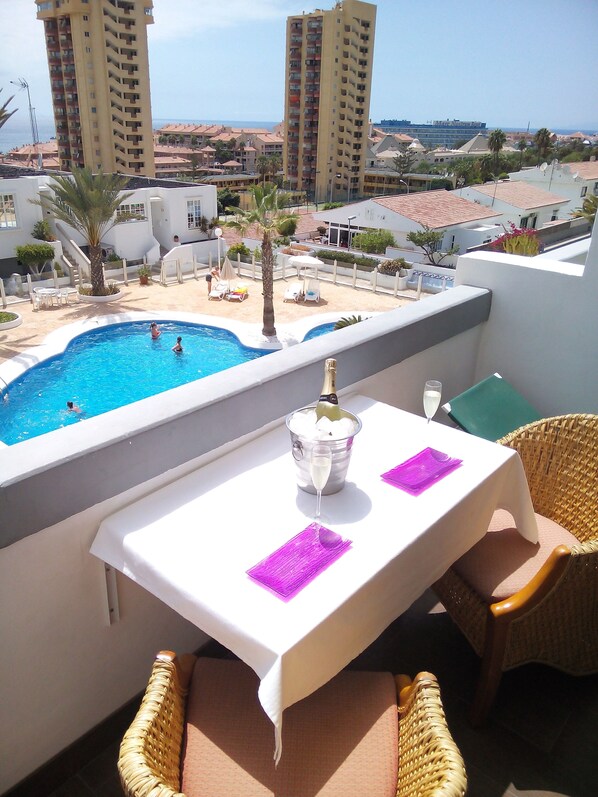 Un balcon avec une piscine, des fauteuils en osier, une table avec une bouteille de champagne et une vue sur la mer et les bâtiments.