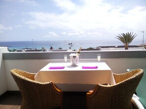 Une table avec une bouteille de champagne, deux verres et une serviette violette, sur un balcon donnant sur la mer.