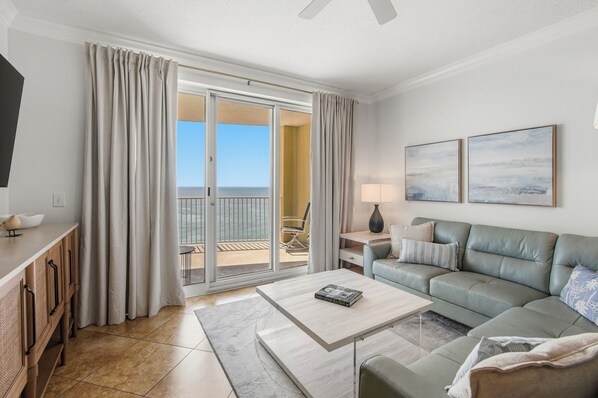 Uma sala de estar moderna com sofá, mesa de centro, TV e vista para o mar através de uma porta de vidro deslizante.