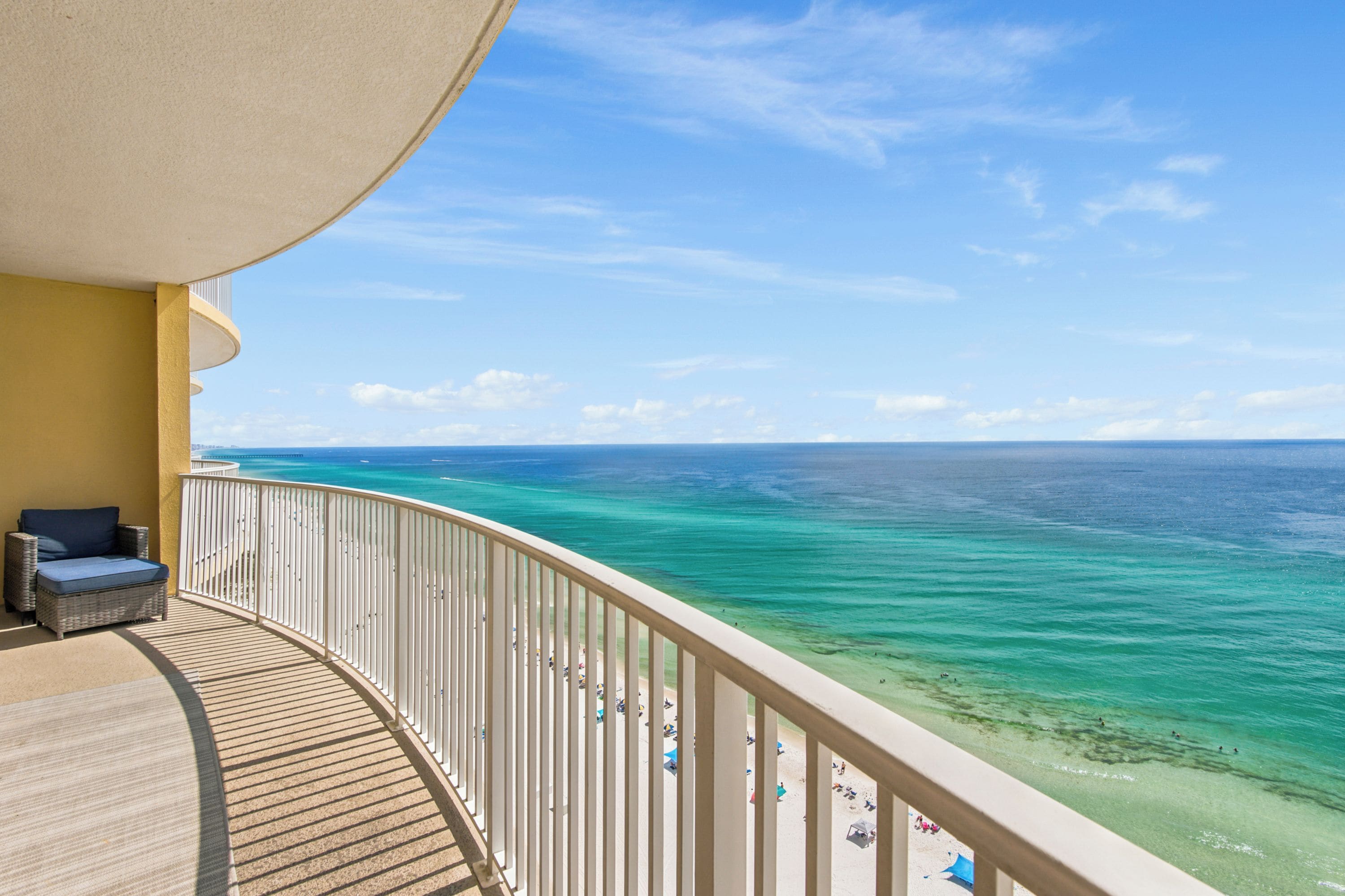 A balcony with a view of the ocean, a wooden deck, and a lounge chair.