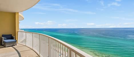 A balcony with a view of the ocean, a wooden deck, and a lounge chair.