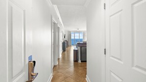 A hallway with white doors, a kitchen area with a window, and a trash can. - Emerald Isle 1708 Just Remodeled! Stunning! Front Row Beach Chairs Included! (Panama City Beach)