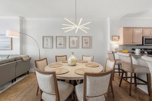 Uma sala de jantar com uma mesa redonda, cadeiras, um vaso e impressões botânicas emolduradas na parede.