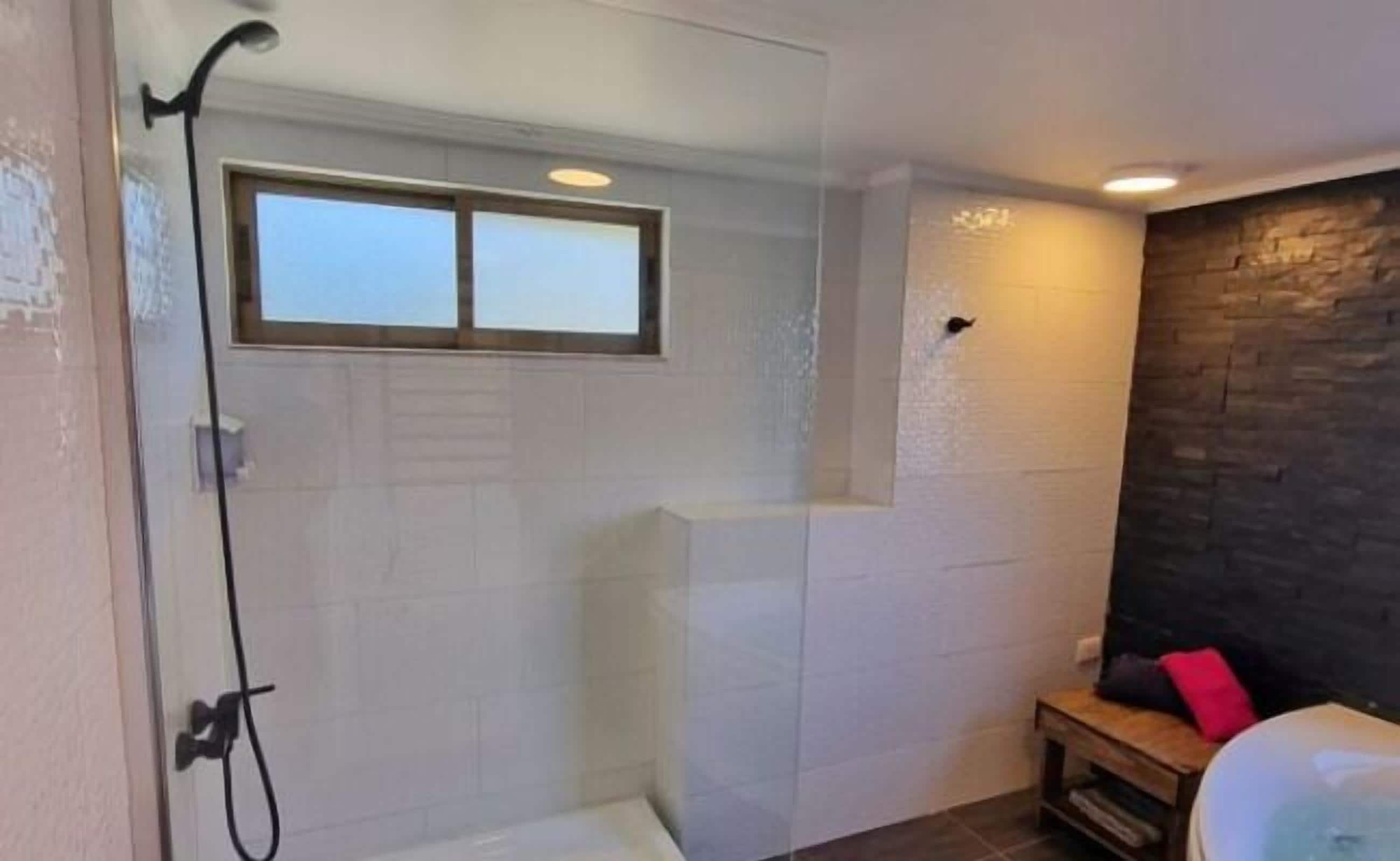 A modern bathroom with a glass shower enclosure, a bathtub, and a small wooden bench.