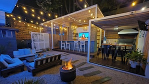 Un patio al aire libre con un pozo de fuego, asientos, una zona de bar y una parrilla.