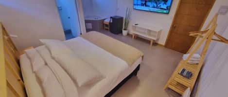 A bedroom with a bed, a TV, a wooden chair, and a desk.