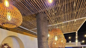 Una barra de madera con lámparas colgantes, estantes con cristalería y un pilar grande.