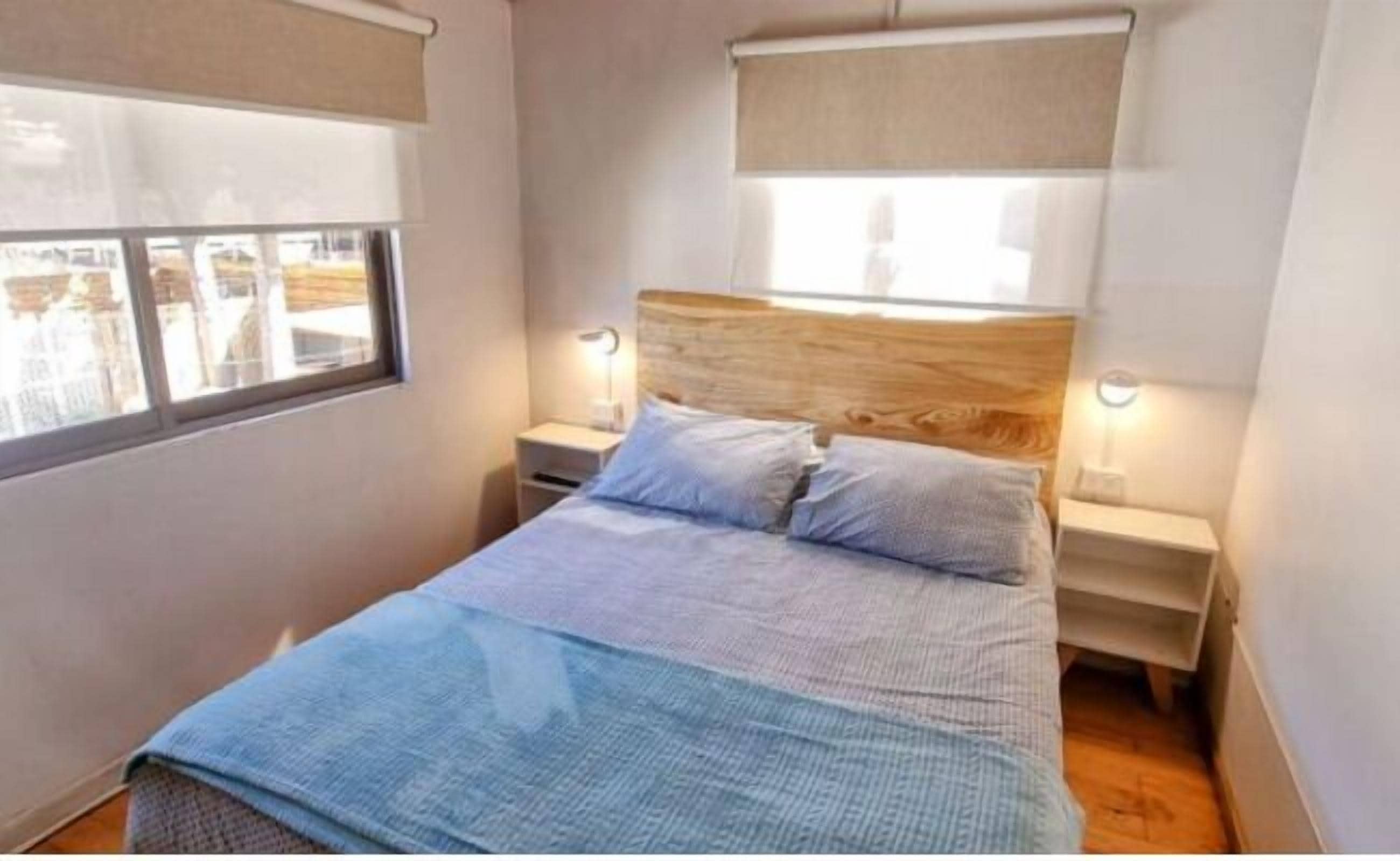 A bedroom with a bed, two bedside tables, a headboard, and a window with blinds.