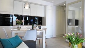 A modern kitchen with white cabinets, a dining area with a white table and chairs, and a living area with a sofa and a vase of flowers. - Villa King (Dubrovnik)