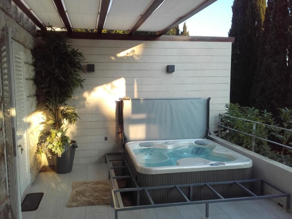 Un bain à remous dans un espace extérieur abrité, avec un mur blanc et une plante en pot.