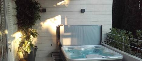 Un bain à remous dans un espace extérieur abrité, avec un mur blanc et une plante en pot.