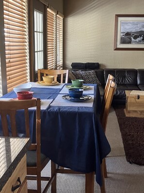 Ein Essbereich mit einem Tisch für vier Personen, Holzstühle und eine Couch im Hintergrund.