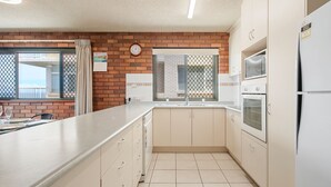 Eine Küche mit Backsteinwand, einer Uhr, einem Fenster mit Jalousien und einem Kühlschrank.