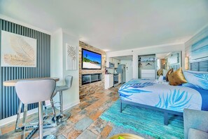 Une chambre d’hôtel moderne dotée d’un grand lit, d’une télévision, d’un coin cuisine et d’un espace salon avec une table et des chaises.