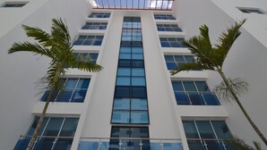 A modern building with a central glass facade, multiple floors, and a flat roof with a skylight.