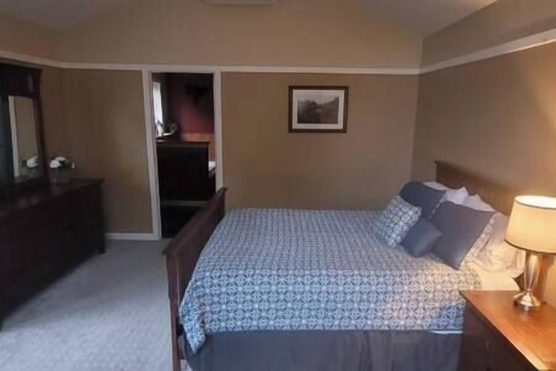 A bedroom with a bed, a dresser, a nightstand, a lamp, and a framed picture on the wall.