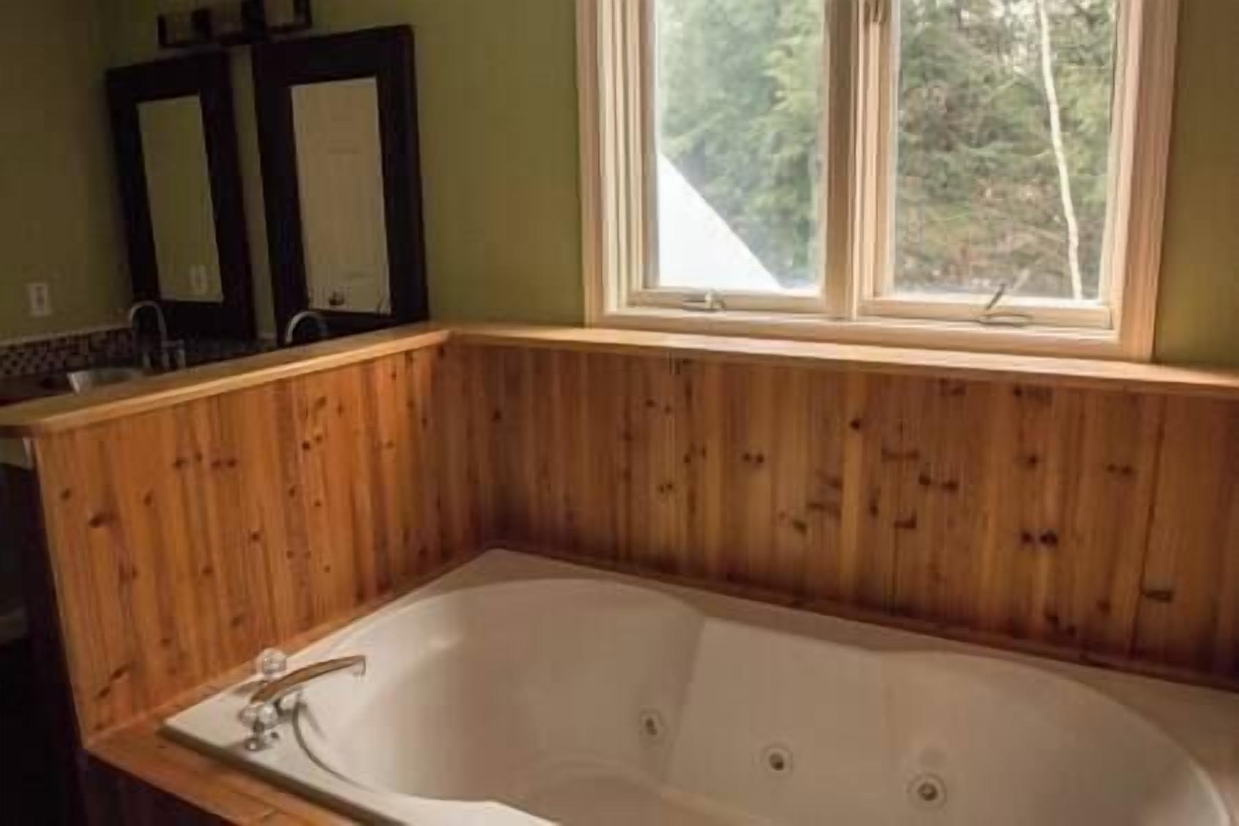 Une salle de bain avec un décor de panneaux en bois, une grande baignoire et une fenêtre donnant sur la forêt.