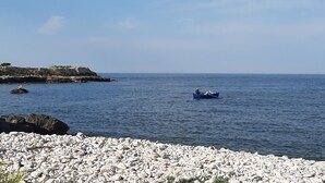 A rocky shoreline with a calm sea, a person in a boat, and a clear sky. - B&B Agorà Bisceglie (Bisceglie)