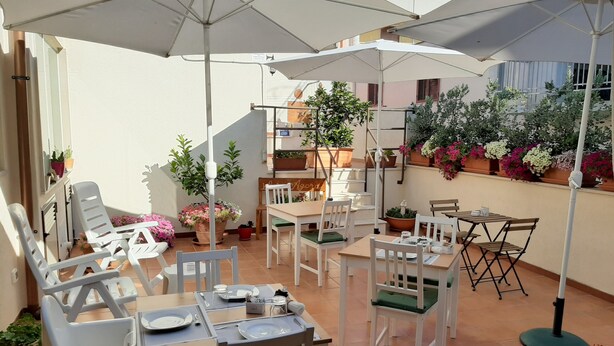 An outdoor patio with multiple tables and chairs, surrounded by potted plants and umbrellas. - B&B Agorà Bisceglie (Bisceglie)