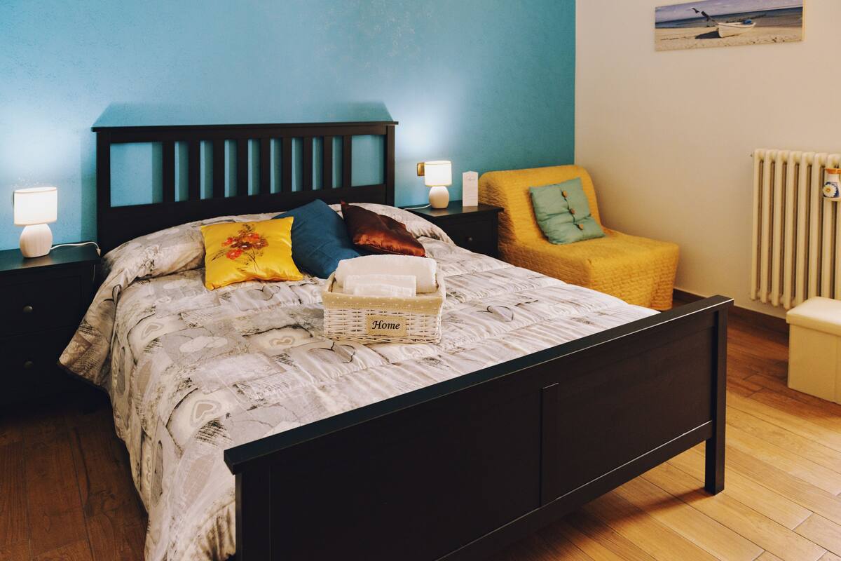 A bedroom with a bed, nightstands, a chair, and a wall with a picture.