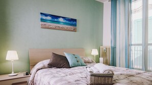 A neatly made bed with a patterned bedspread, two bedside lamps, a wall-mounted painting of a beach, and a window with curtains. - B&B Agorà Bisceglie (Bisceglie)