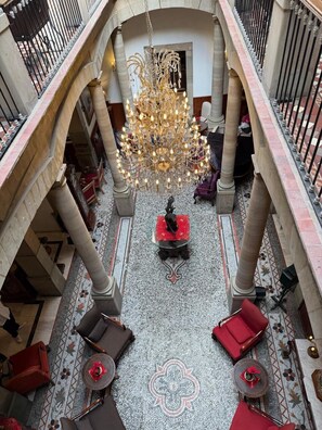 A spacious lobby with a grand chandelier, multiple seating areas, and a decorative floor pattern.