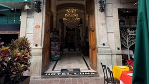 La entrada del Hotel Luna, con una imponente lámpara de araña, un balcón con macetas colgantes y un letrero sobre la entrada.