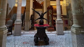 Un lobby imponente con una gran araña, columnas de piedra y una escalera.