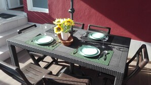 Una mesa para comer al aire libre con cuatro sillas, un florero con girasoles y un mantel individual verde.