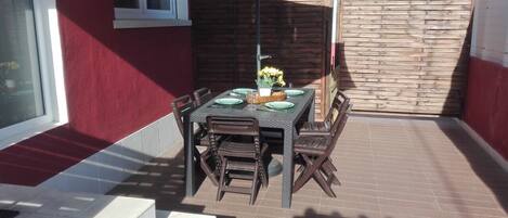 A patio with a table set for four, surrounded by chairs, and a small table with a basket and flowers.