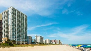 A beachfront hotel with multiple high-rise buildings, a sandy beach, and beach umbrellas. - ***PRICE DROPS, SPECIAL OFFER AUG 24/30*** Summer Get Away before School (Myrtle Beach)