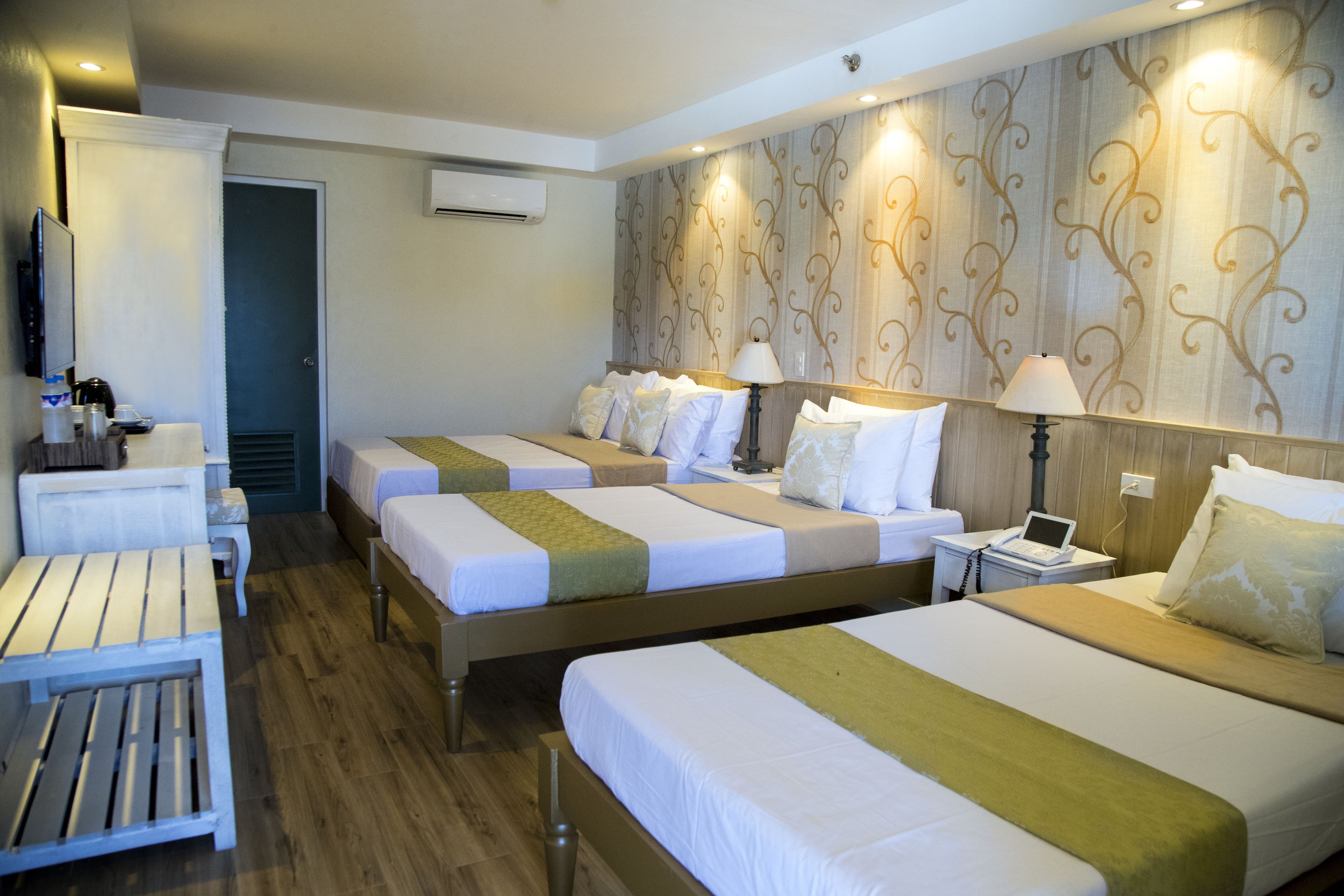 A hotel room with three beds, a desk, a chair, and a TV.