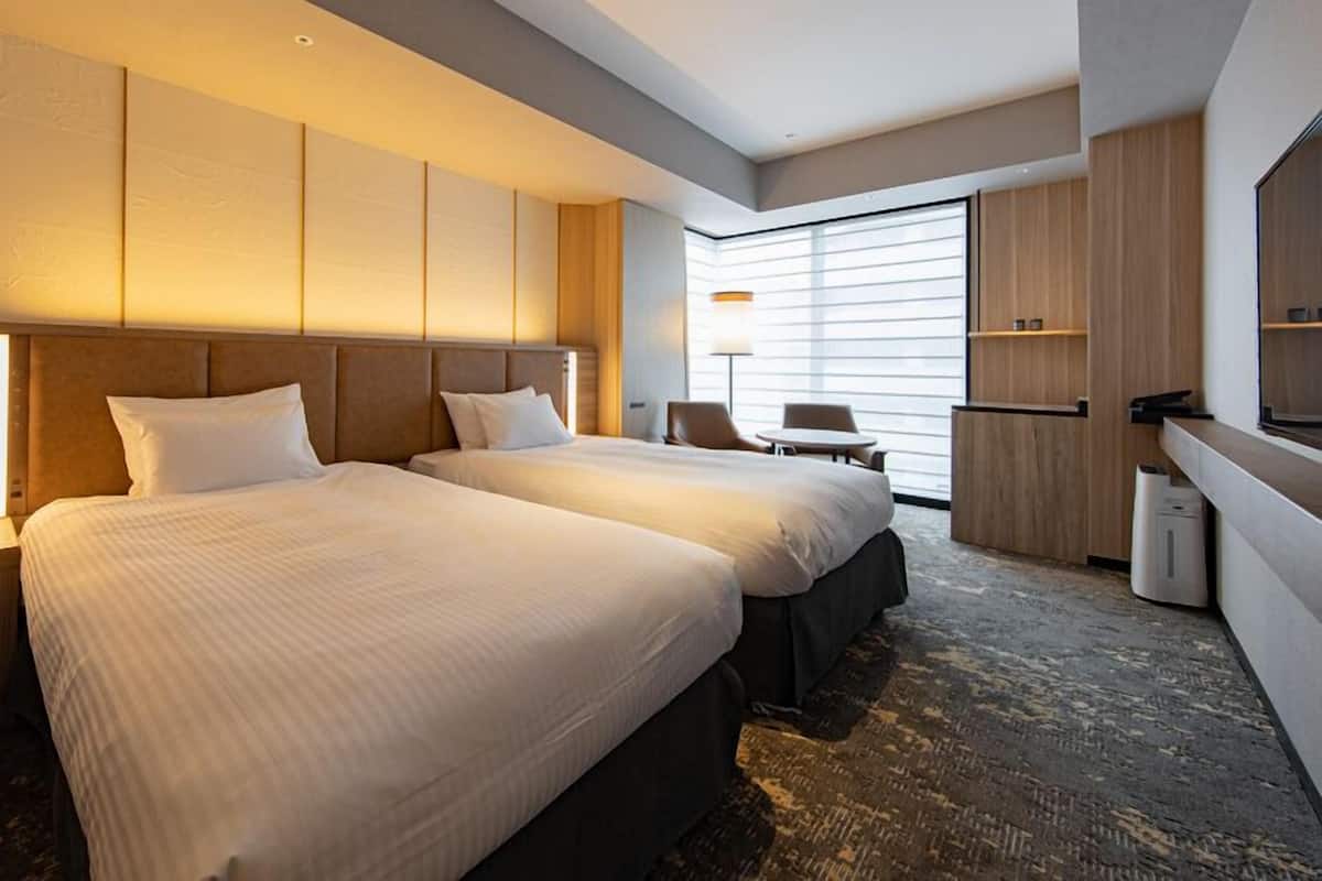 Una habitación de hotel con dos camas, un escritorio, una silla y un ventanal grande.