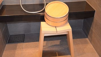 A wooden stool with a round seat in a bathroom with dark tiled walls and a black countertop.