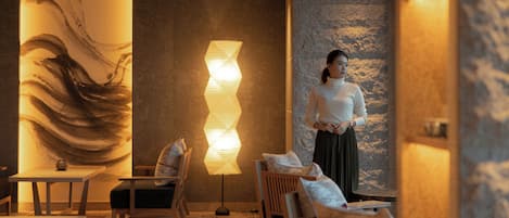Un interior moderno con un cuadro abstracto de grandes dimensiones, una lámpara de pie geométrica y una zona de estar con muebles de madera.
