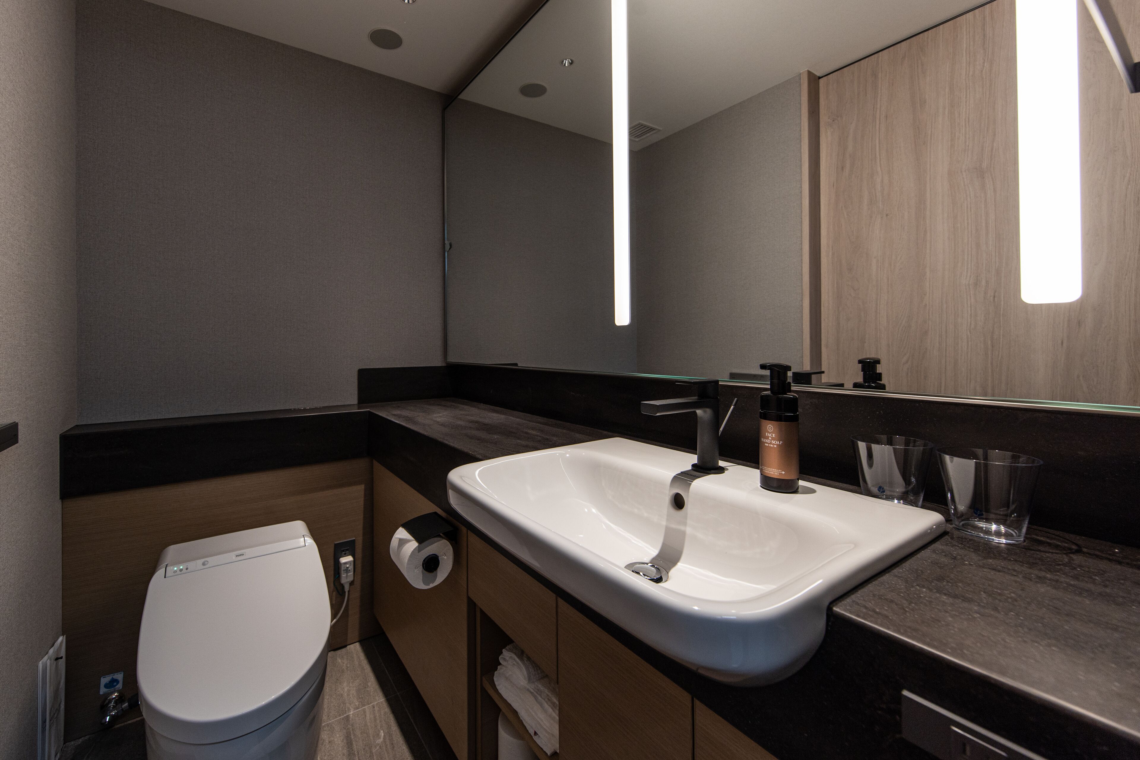 Une salle de bain moderne avec un lavabo blanc, un plan de toilette foncé et des meubles en bois.