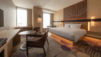 A modern hotel room with a large bed, a desk, a chair, and a small table.
