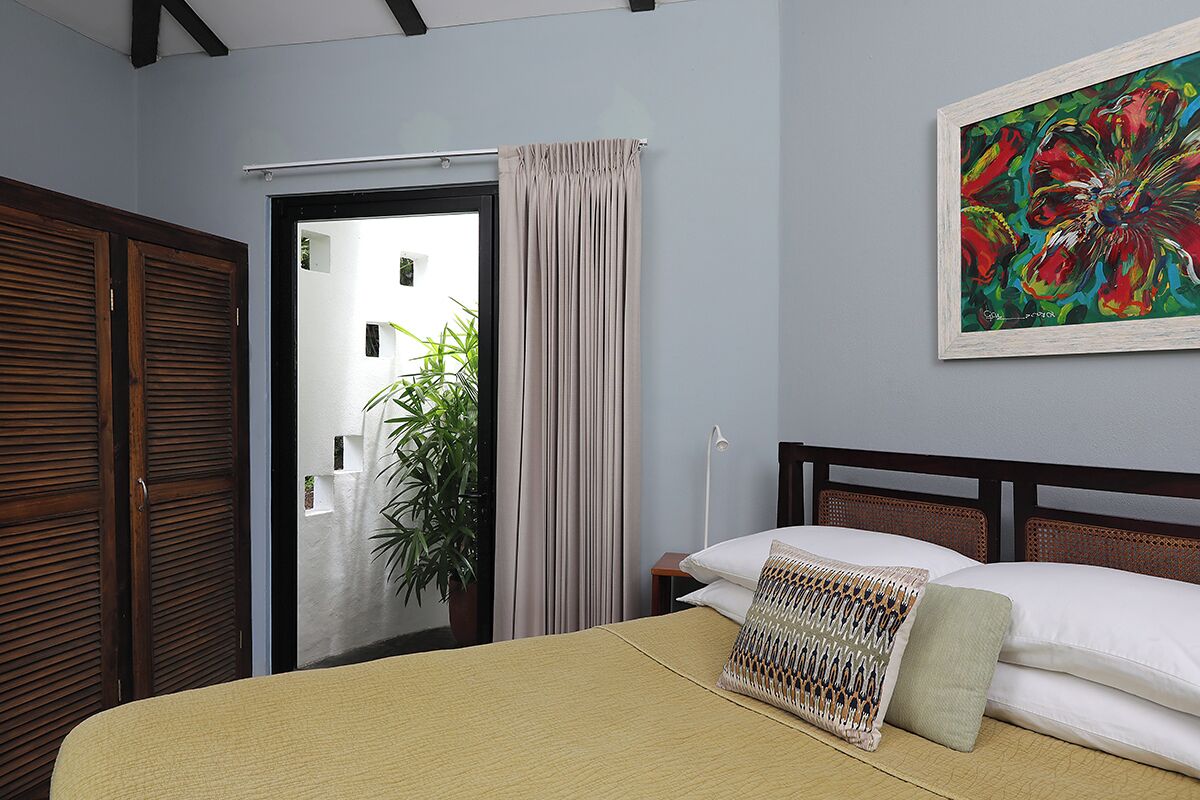 Een slaapkamer met een bed, een schilderij, een raam met gordijnen en een deur.