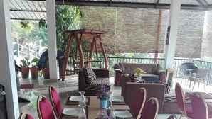 Un lungo tavolo da pranzo apparecchiato per un pasto, con sedie, un composizione floreale al centro e una sedia a dondolo sullo sfondo.
