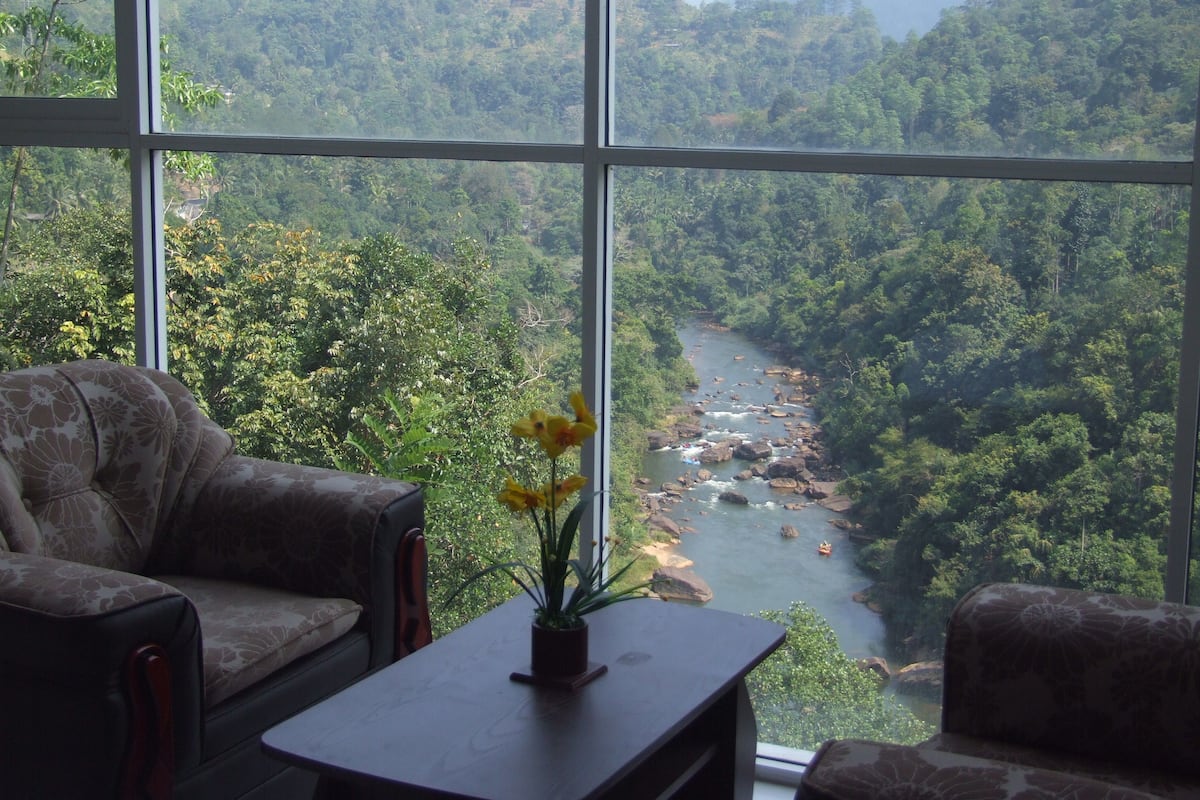 A room with a large window overlooking a river and forested hills.